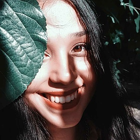 junge asiatische Pfelgerin lächelt mit einem Pflanzenblatt vor dem Gesicht in die Kamera