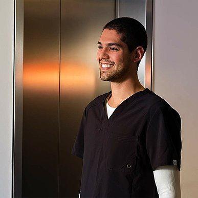 Lächelnder Pfleger vor einem Aufzug