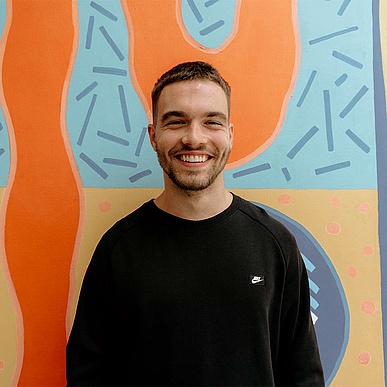 professional stands in front of a colourful wall at work and smiles