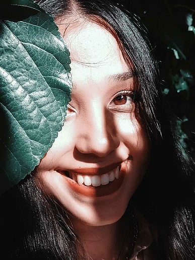 Joven asiática sonríe a la cámara con una hoja de planta frente a su cara